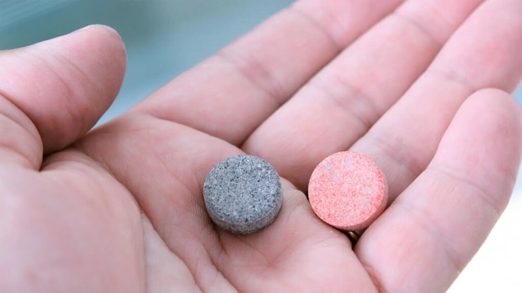A photo of two antacid tablets in a man’s hand.