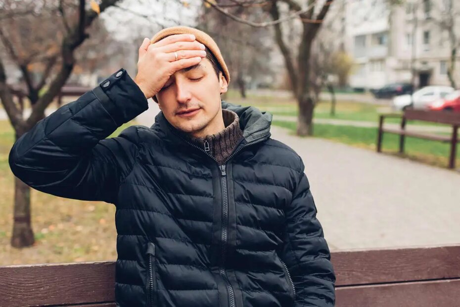 A sick man with a headache and fever sitting on a bench in Fall.