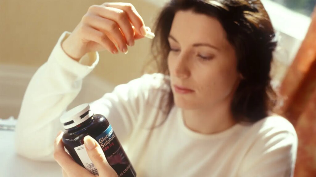 Dementia May Be Worse for People Taking Popular Supplement A photo of a woman holding two glucosamine capsules and the bottle they came from.