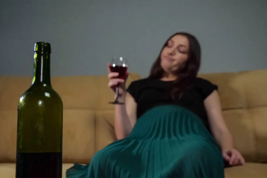A photo of a pregnant woman sitting on a couch and holding a glass of red wine.