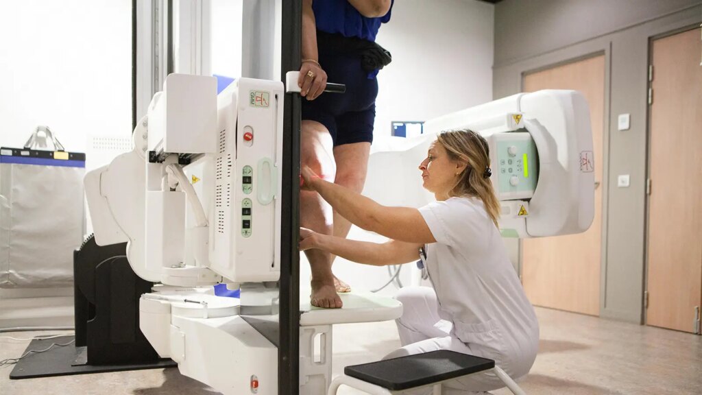 GLP-1 Drugs Cut Need for Knee Replacement A photo of a female radiologist preparing her mature female patient for a knee x-ray.