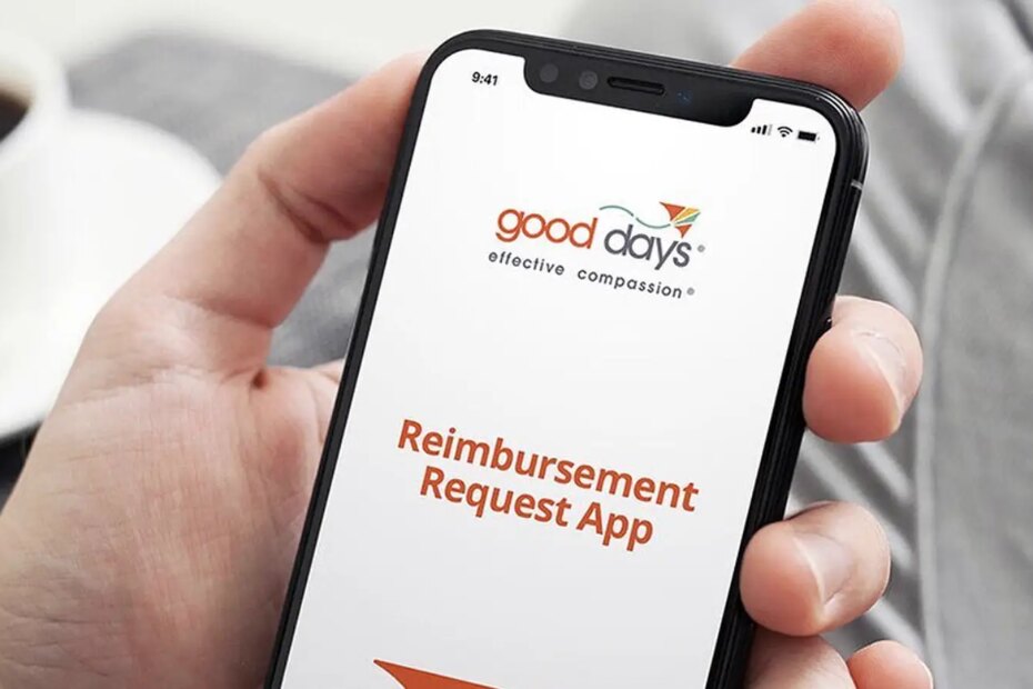 A photo of a man holding a smartphone displaying the Good Days reimbursement app.