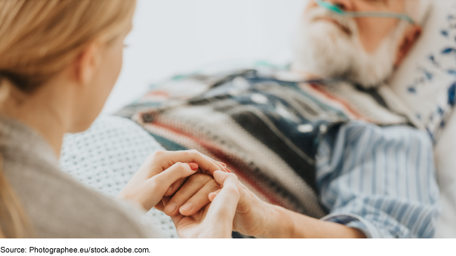 Medicare Hospice: Action Needed to Pay More Efficiently for Routine Home Care A woman holding the hand of an older man who is receiving supplemental oxygen from a medical device while in bed.