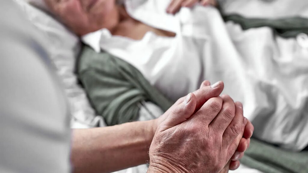Nearly a Third of Americans Will Live in States With Legal Aid in Dying by September A photo of a senior man at the bedside of his wife and holding her hand.
