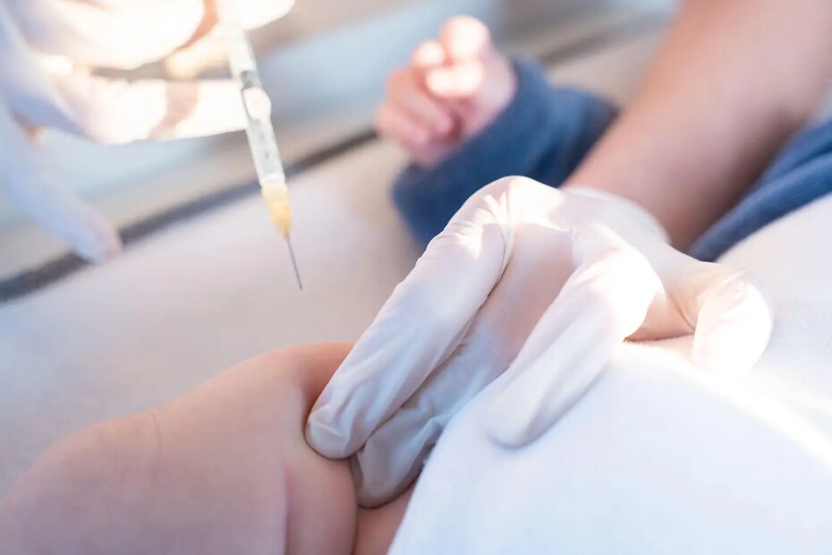 A photo of a physician preparing to give a newborn a shot in the leg.