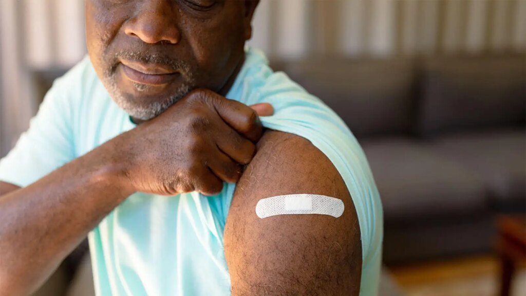 Shingles Vaccine Might Be Less Effective in Systemic Sclerosis Patients A photo of a mature man lifting his sleeve to reveal a vaccination Band-Aid.
