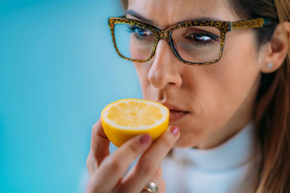 A photo of a woman attempting to smell half of an orange.