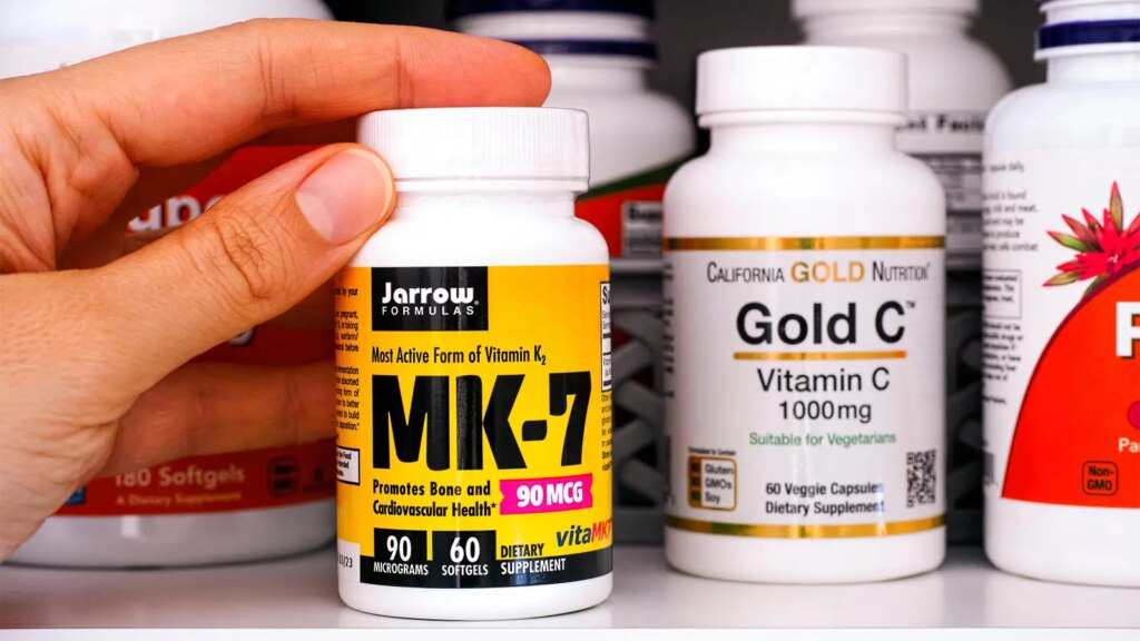 Trial: Vitamin K Supplement Curbs Coronary Atherosclerosis A photo of a woman’s hand on a bottle of vitamin K MK-7 supplements.