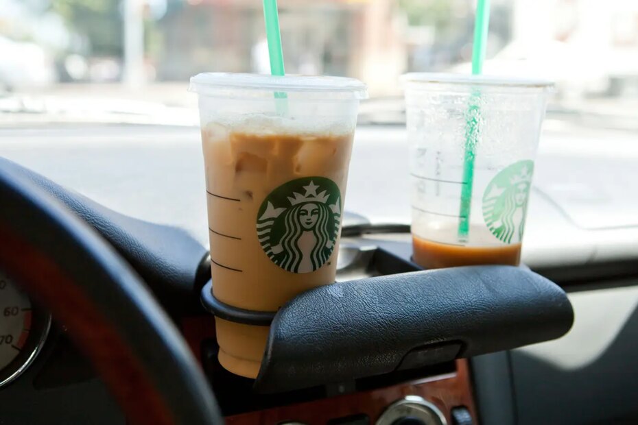 A photo of two plastic cups of Starbucks coffee in car cup holders.