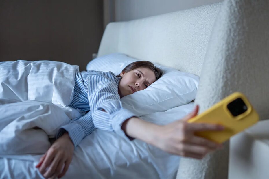 A photo of a woman lying in bed and checking her smartphone.