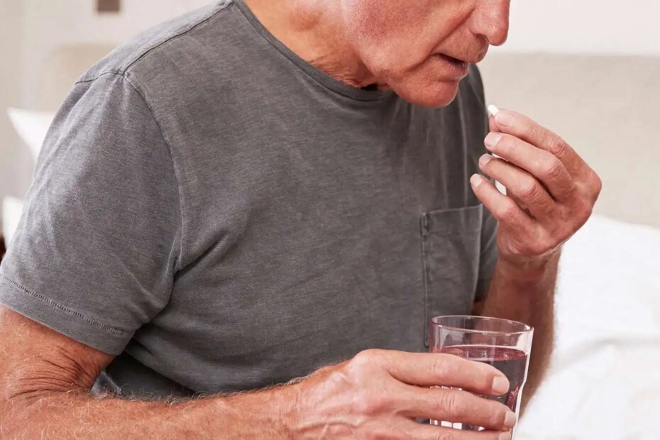 Senior man sitting on a bed taking medication.
