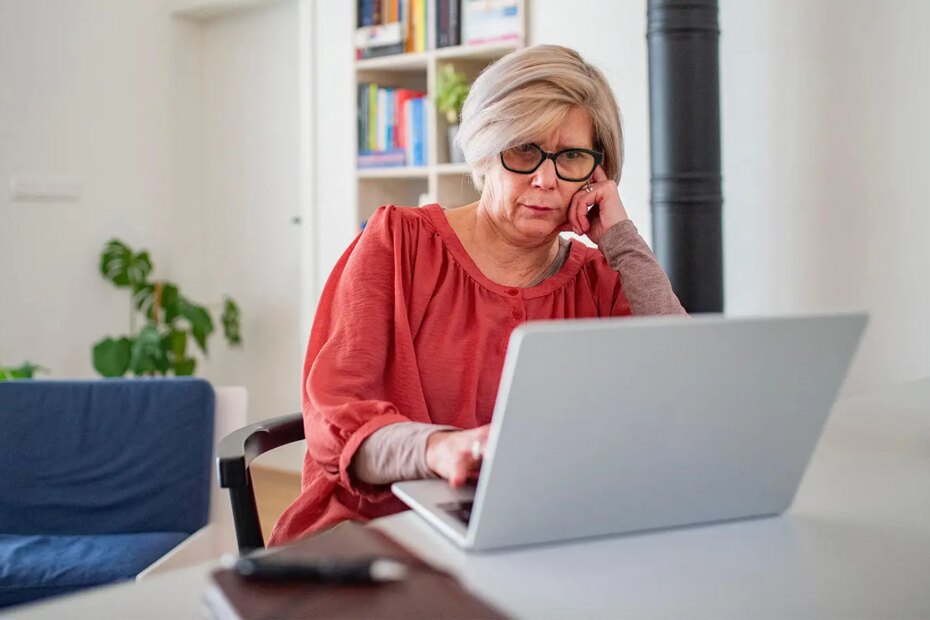 A photo of a senior woman at home looking at a laptop.