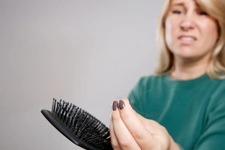 A photo of a stressed looking woman holding a hair brush and some of her hair.