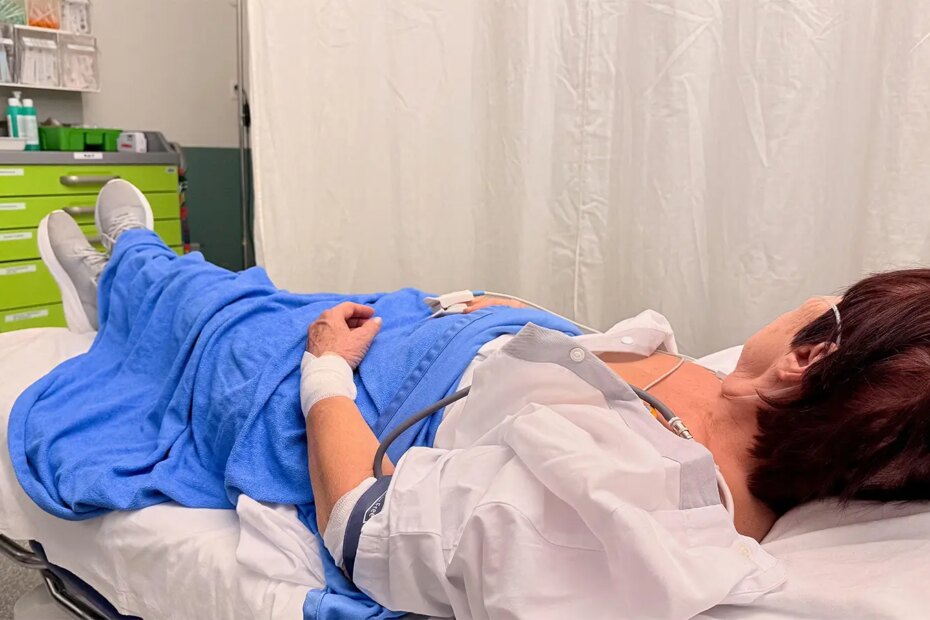 A photo of a mature woman lying on a bed in a hospital emergency department.