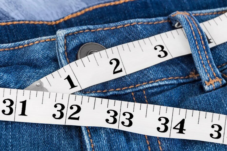 A photo of a measuring tape threaded through the belt loops of a pair of jeans.
