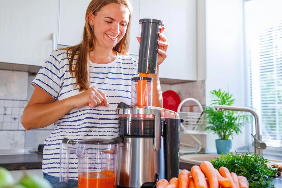 A photo of a smiling woman making carrot juice in her kitchen.