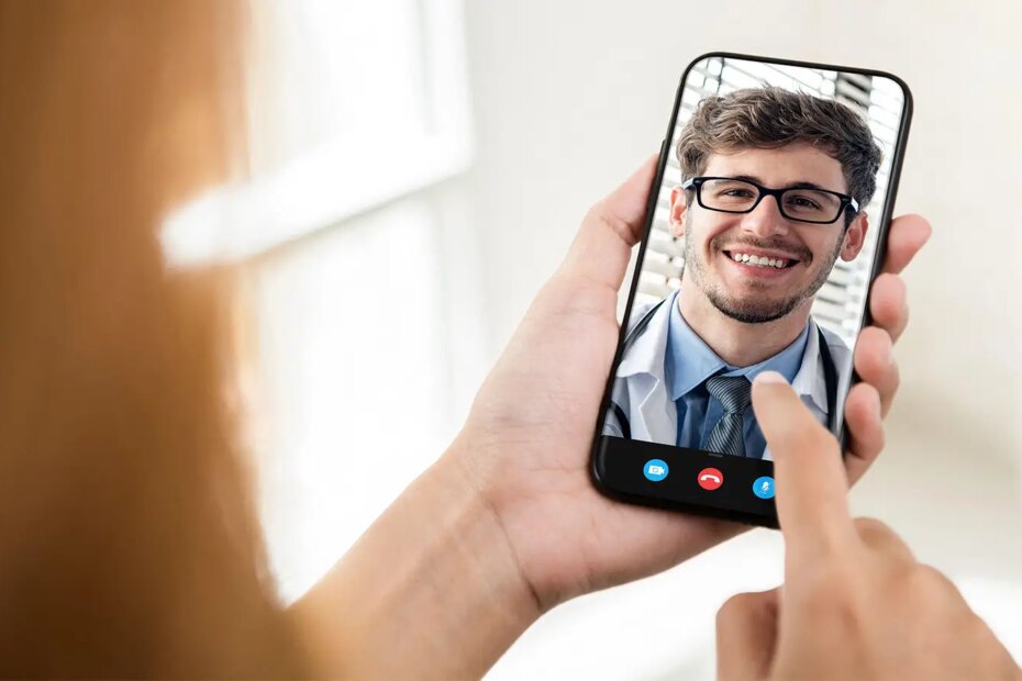 A photo of a woman holding a smartphone displaying a male physician.