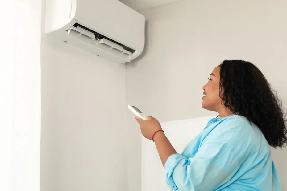 A photo of a woman using a remote to turn on a wall mounted air conditioner.