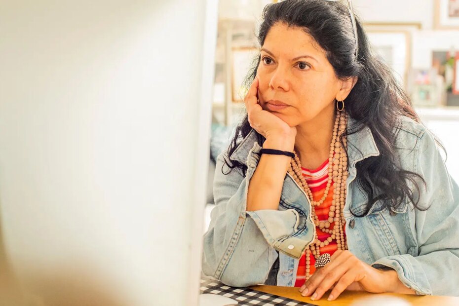 A photo of a mature woman at home looking at a computer monitor.