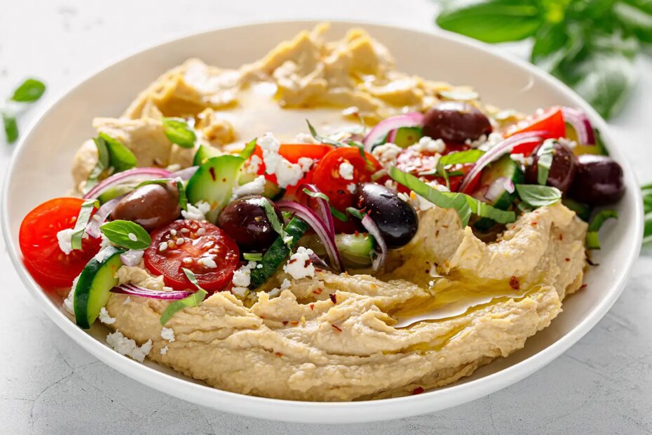 A photo of a bowl of hummus, olives, tomatoes, onion, cucumber, and feta.