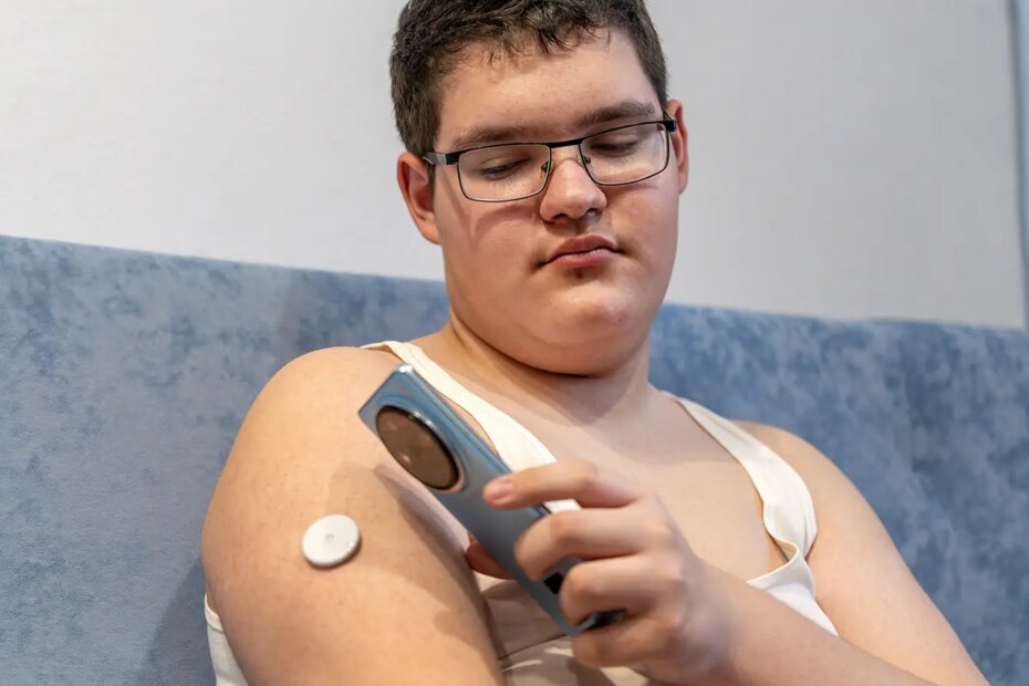 A photo of a teen male checking his continuous glucose meter with a smartphone.