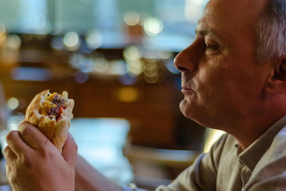 A photo of a senior man eating a large hamburger.