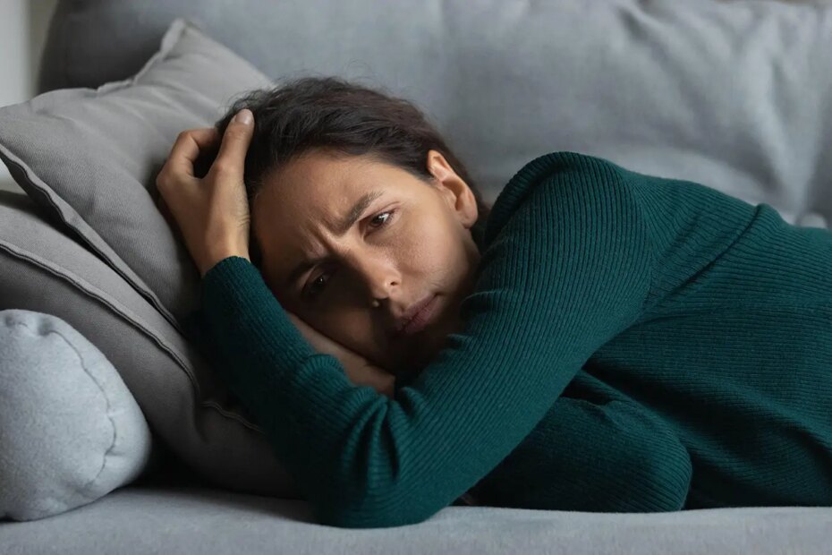 A photo of a frowning woman lying on a couch.